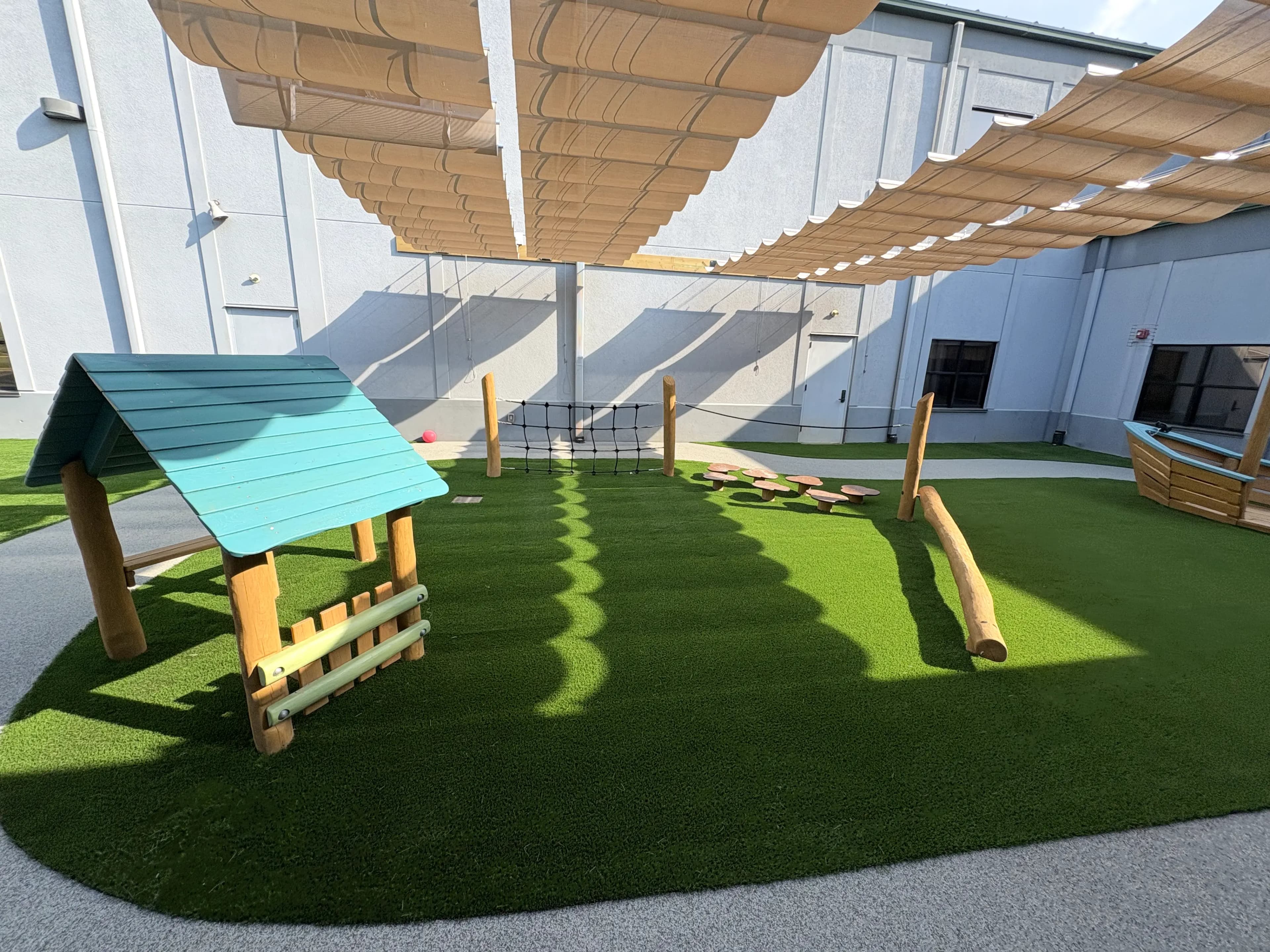 Grace Covenant Church covered playground area with small log playhouse and balance beam on artificial turf