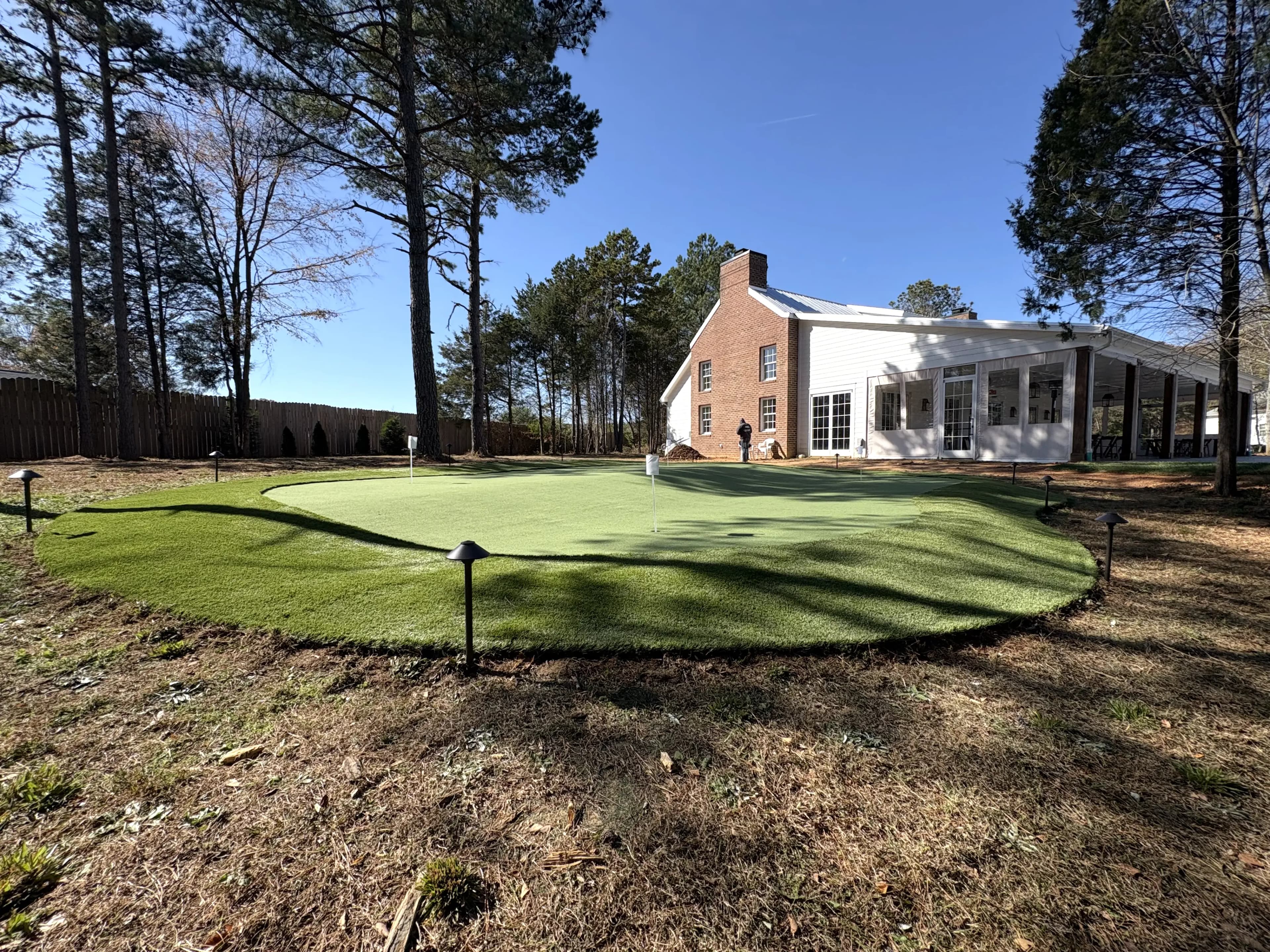 Multi-hole putting green with fringe turf and landscape lighting at brick farmhouse estate