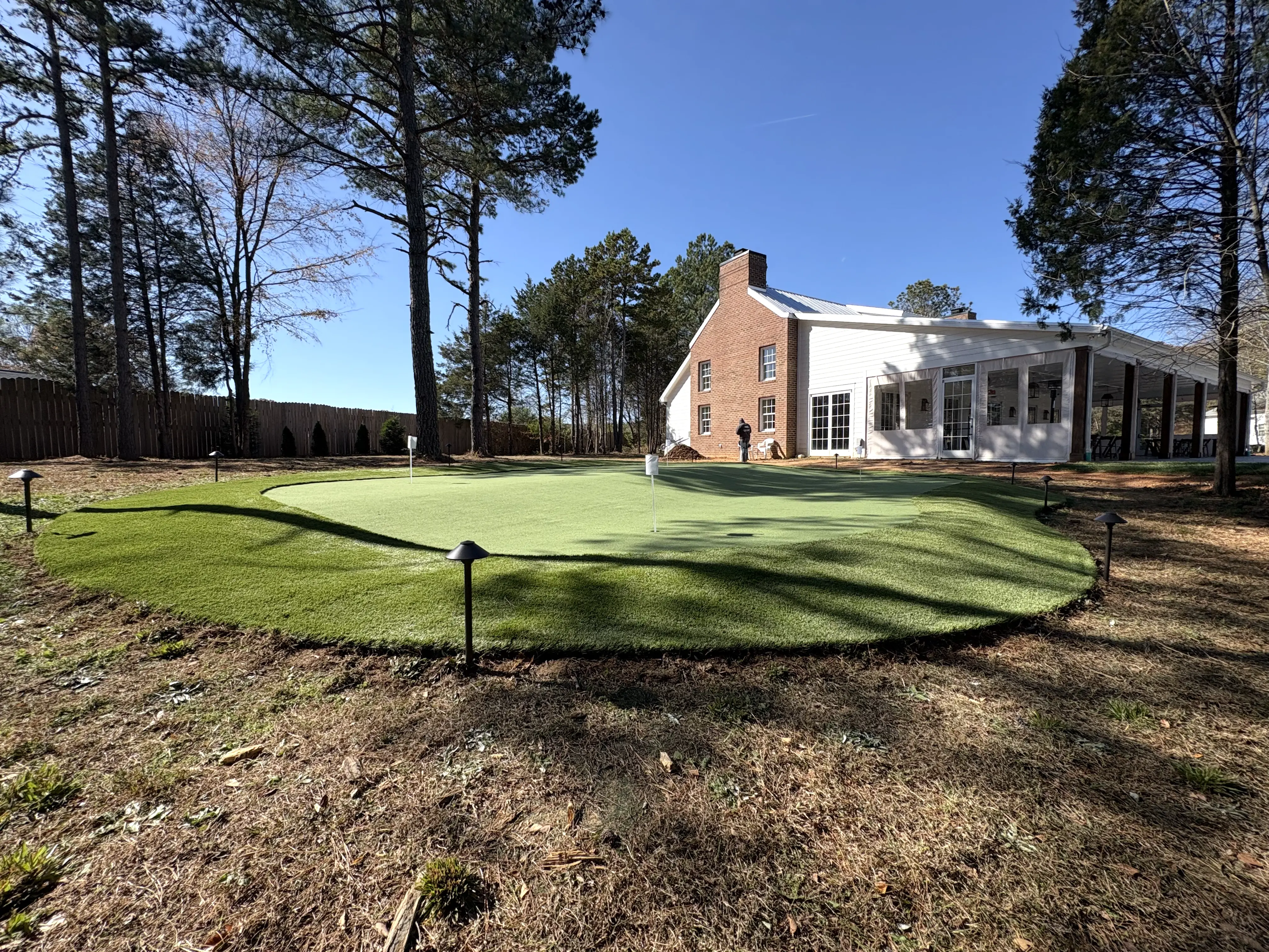 Multi-hole putting green with fringe turf and landscape lighting at brick farmhouse estate